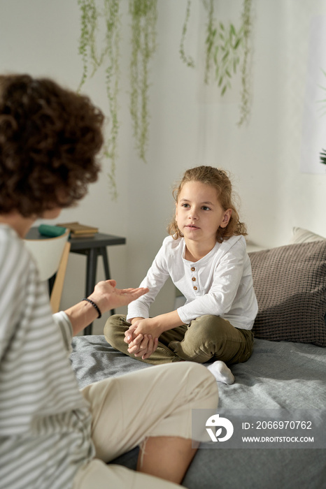 Little boy sitting on bed and listening to his mom while she talking to him about his behavior