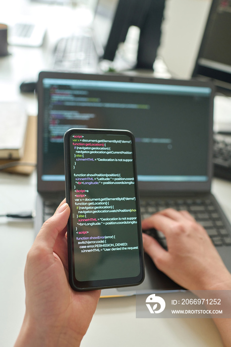 Close-up of programmer using computer codes on his smartphone to install software program on laptop