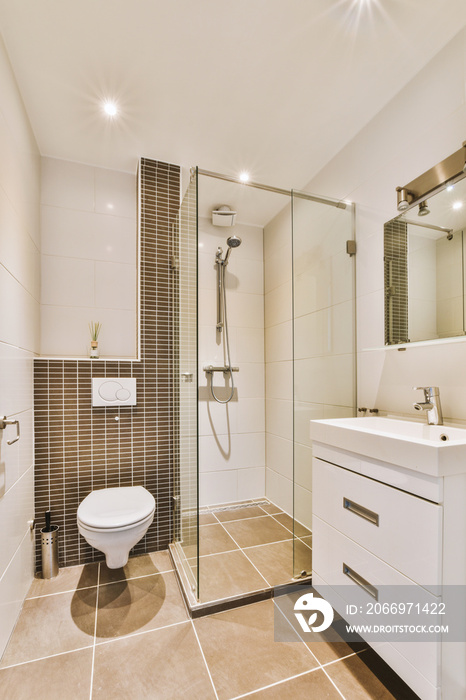 Flush toilet located between sink and shower in small tiled bathroom of contemporary apartment