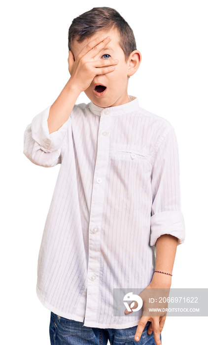 Cute blond kid wearing elegant shirt peeking in shock covering face and eyes with hand, looking through fingers with embarrassed expression.