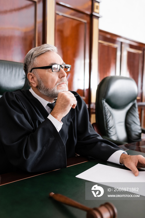 senior judge in robe and eyeglasses sitting with pen during litigation