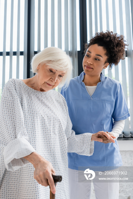 African american nurse holding hand of senior patient with walking cane