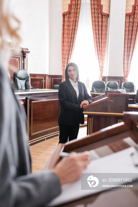 brunette witness looking at blurred attorney writing during litigation