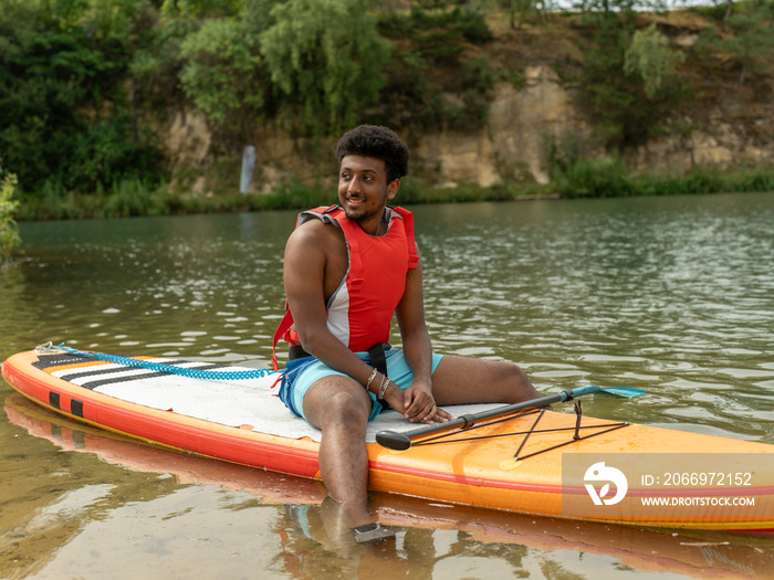 Young man sitting on paddleboard on lake