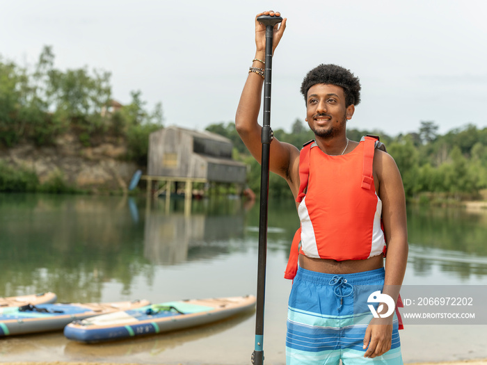 Portrait of young man standing with oar by lake