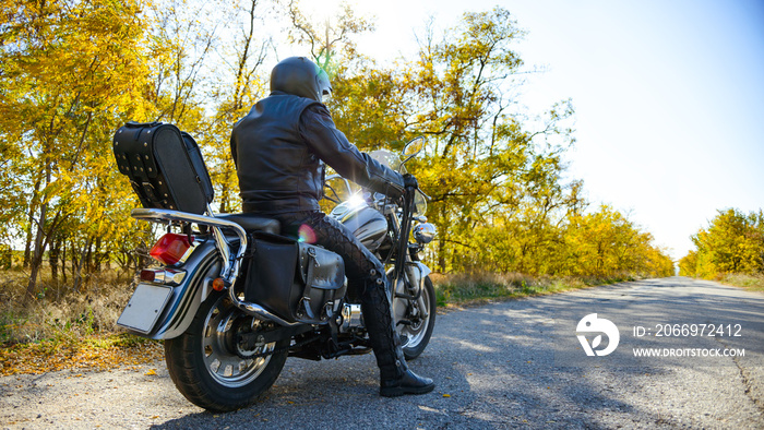 Motorcycle Driver Riding Custom Chopper Bike on Autumn Road. Travel and Adventure Concept.