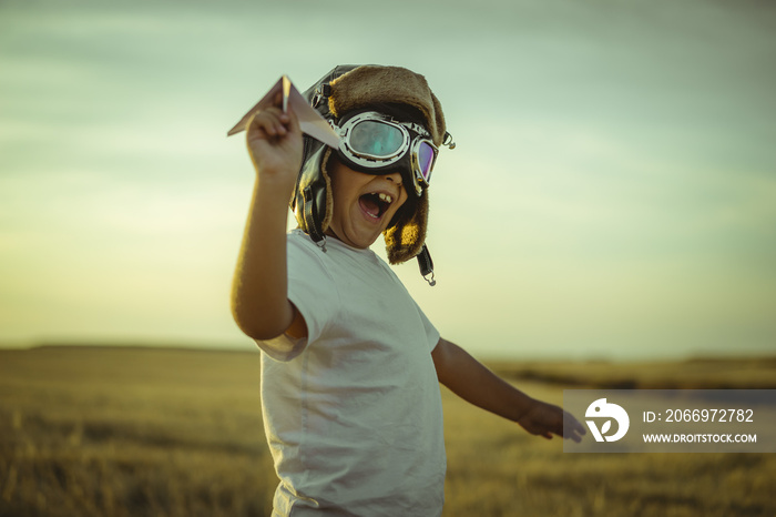 Happy boy at sunset playing at being aviator, he wears pilot glasses of airplanes and some cardboard like wings