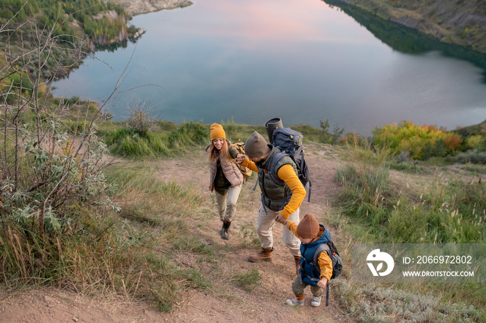 Family of hikers with backpacks climbing mountain against river during trip