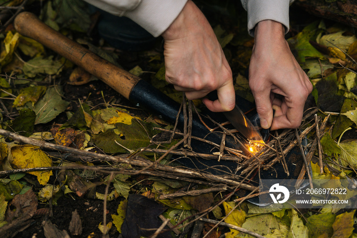 Close-up cropped shot of scout male lighting fire, starting campfire with fire starting tools and knife. Traveler tourist striking ferrocerium rod to make bonfire on hiking adventure.