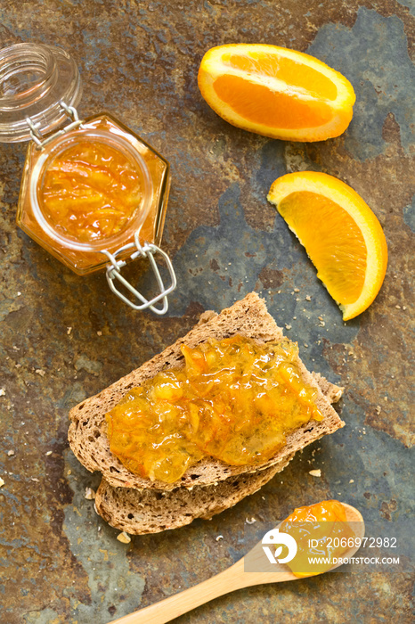 Orange jam on wholegrain bread slices, photographed overhead on slate with natural light (Selective Focus, Focus on the orange jam on the bread)