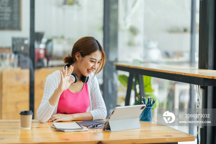 Young adult happy smiling Asian student wearing headphones talking on online chat meeting using laptop in university campus or at virtual office. College female student learning remotely.