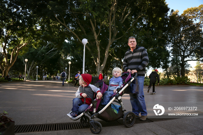 Father pushing two little boys in double pram while exploring Hyde Park in Sydney, NSW Australia