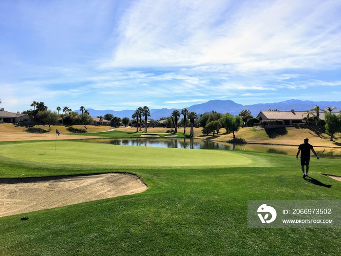 A young male golfer walking towards the green on a par 4 surrounded by water on a golf course in the desert oasis of Palm Springs, California, United States of America.