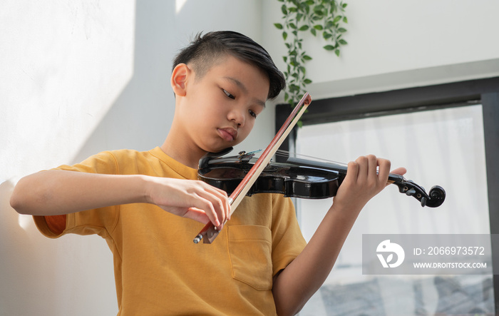 A Little Asian kid playing and practice violin musical string instrument against in home, Concept of Musical education, Inspiration, Teenager art school student.