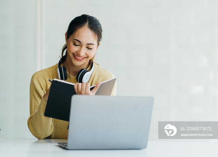 Smiling Asian young female using headset looking at laptop screen listen and learning online courses. Happy asian business woman with headphones video call for customer service.