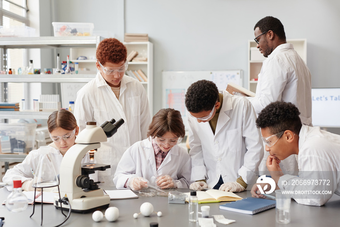 Front view at diverse group of smiling children enjoying experiments with microscope in chemistry lab at school