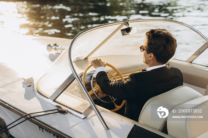 Business portrait of young man in suit and sunglasses posing on a yacht in a daylight sun