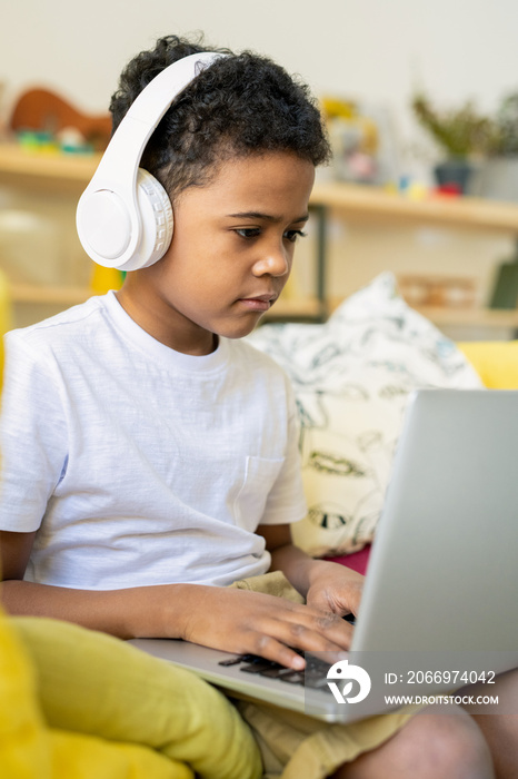 Elementary schoolboy of African ethnicity with headphones typing on laptop