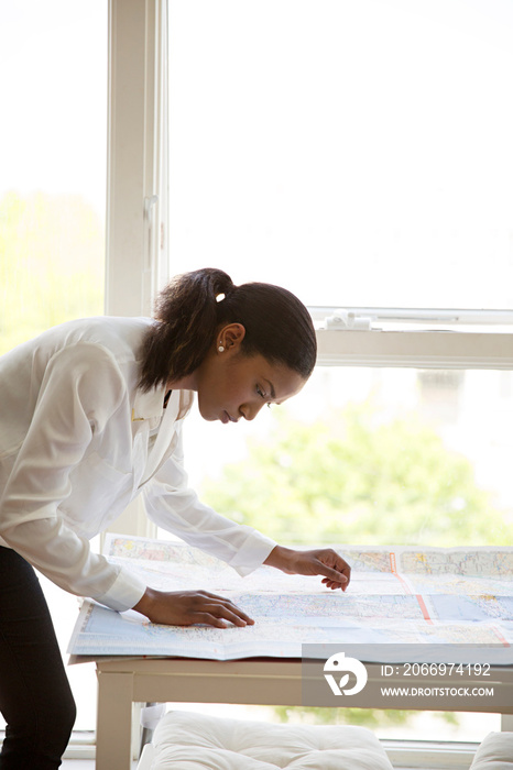 Concentrated businesswoman reading map at table against windows