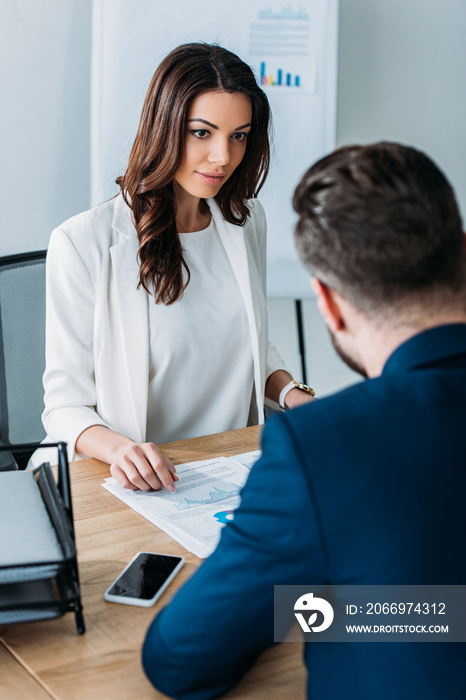 selective focus of attractive advisor and investor in suits discussing document at office