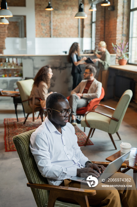 Serious African businessman using laptop against busy colleagues