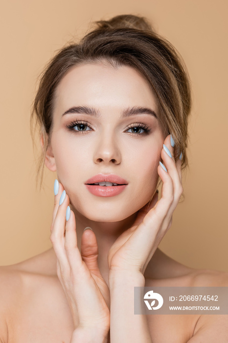 pretty woman with clean skin and natural makeup touching face isolated on beige.