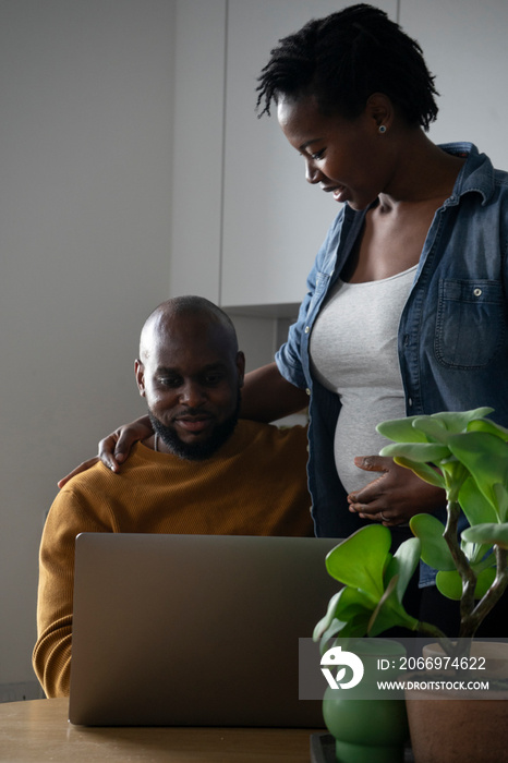 Man and pregnant woman looking at laptop in kitchen