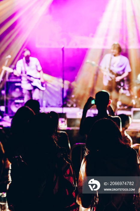 Concert crowd attending a concert, people silhouettes are visible, backlit by stage lights