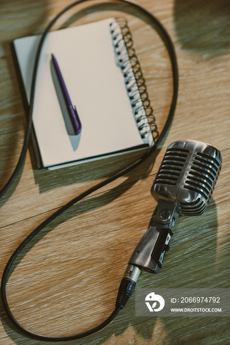 Top view of wired retro microphone lying on wooden table with blank notebook