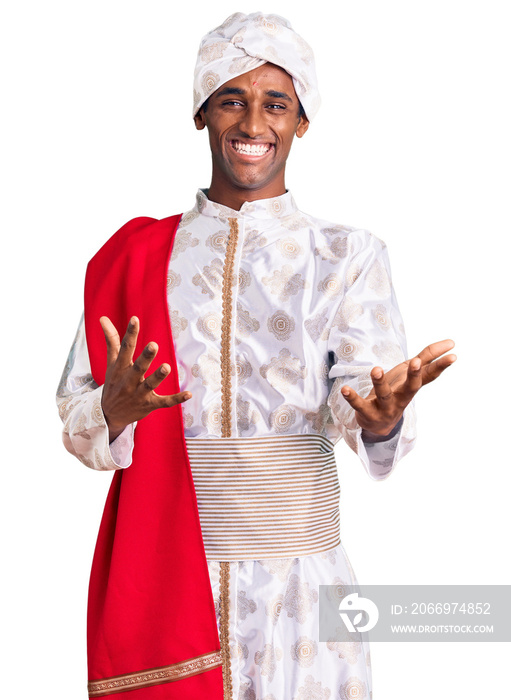 African handsome man wearing tradition sherwani saree clothes smiling cheerful with open arms as friendly welcome, positive and confident greetings