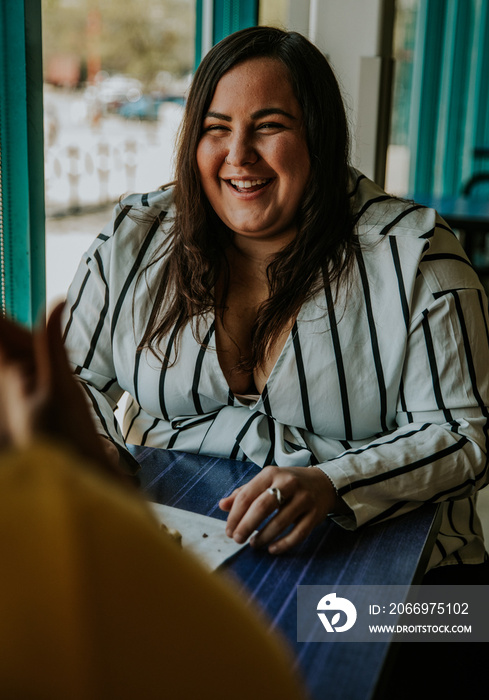 2 plus size women sit at table and laugh