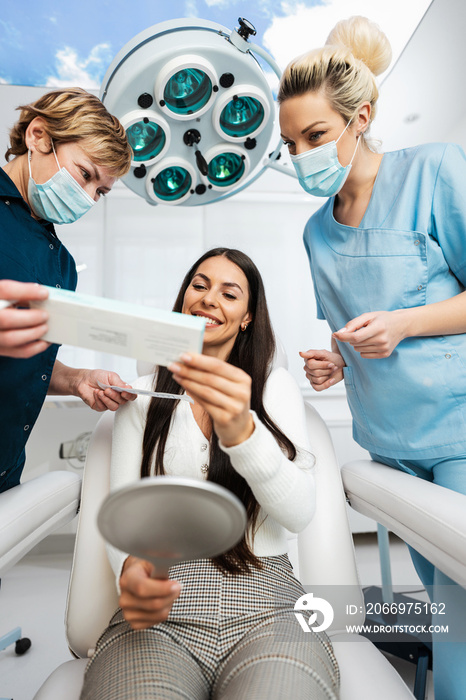 Beautiful and happy brunette woman at beauty medical clinic. She is sitting and talking with two female doctors about face aesthetic treatment.