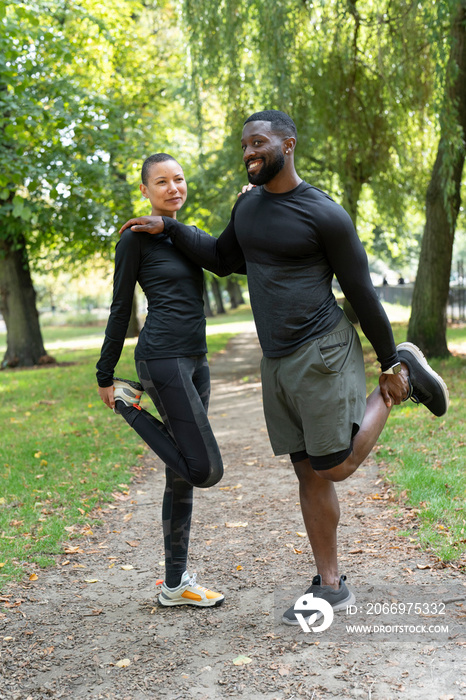 Portrait of smiling man and woman stretching legs in park