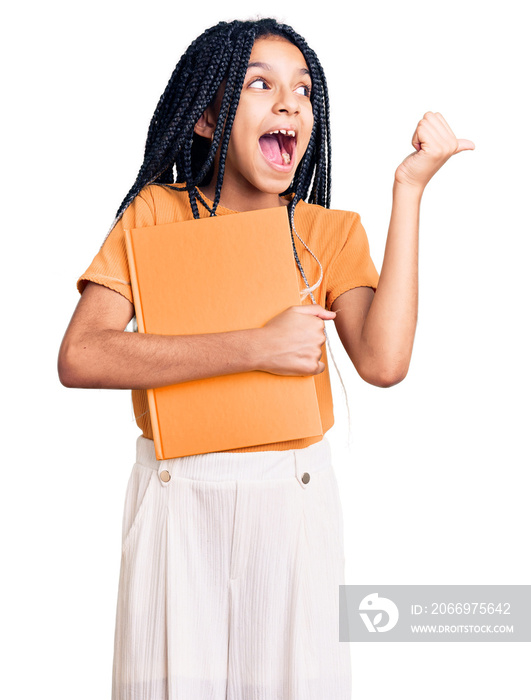 Cute african american girl holding notebook pointing thumb up to the side smiling happy with open mouth