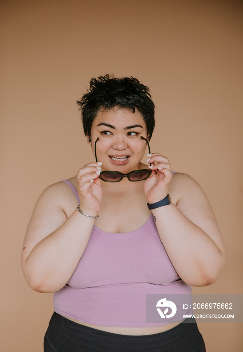 portrait of a plus size filipino woman holding sunglasses looking playful