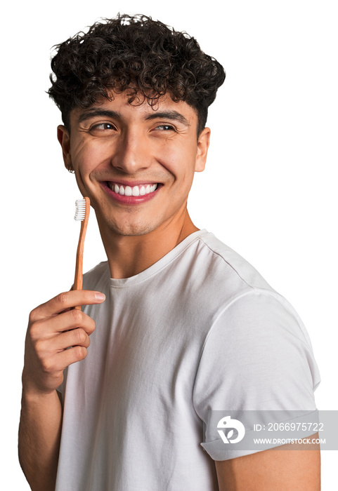 A young latin man brushing with a wooden teethbrush looks aside smiling, cheerful and pleasant.