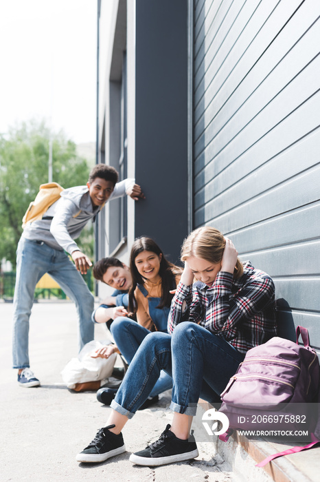 pretty and smiling friends bulling and pointing with fingers at sad blonde teen