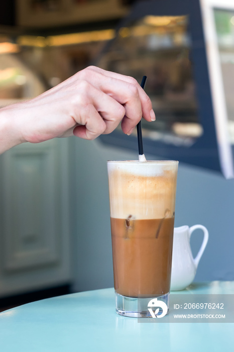 Female hand stirring a straw on a greek cold coffee, freddo cappuccino, outdoors.