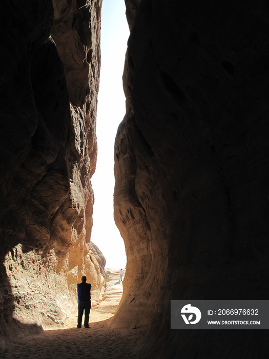 The silhouette of a man against the light in the middle of a passage between two huge rocks. Madain Saleh, archaeological site with Nabatean tombs in Saudi Arabia (KSA)