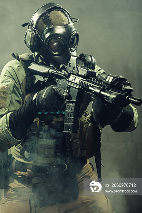 Special unit soldier with gasmask and tactical equipment is holding assault rifle.