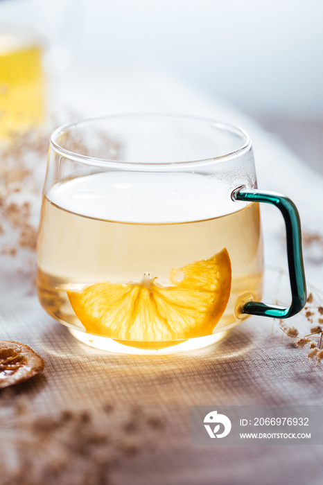 Cup of chamomile tea in transparent mug served with slice of lemon and orange. Tea break.