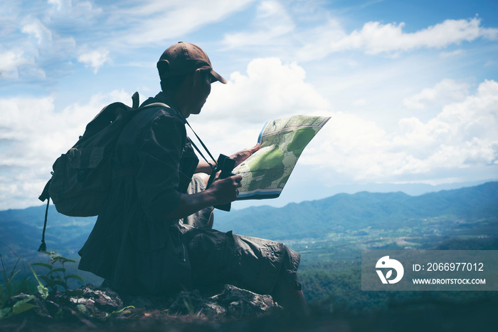 Young male hiker hand holding map and binoculars with backpack relaxing on top of a mountain - scenery from vacation - photo with space for your montage.