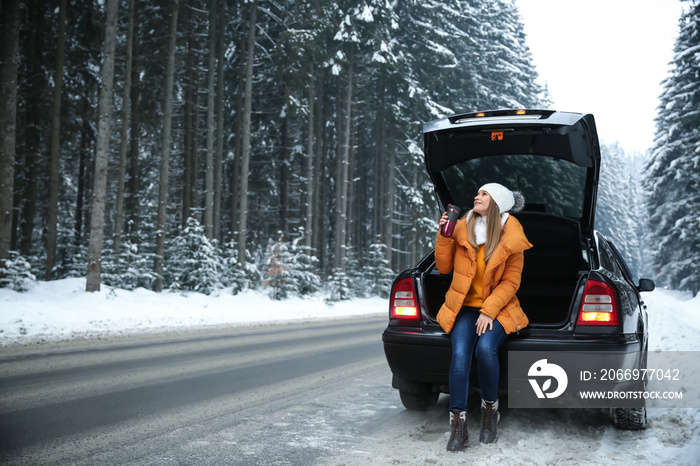 Young woman with hot drink near car at winter resort