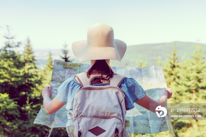 Hiking woman traveler with backpack checks map to find directions in wilderness area, real explorer - focus on hat - shallow depth of field. Vintage filter applied. Travel Concept