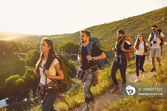 Group of young hiking friends with large backpacks on their shoulders climbs to the top of the mountain in the sunset light. Concept of active tourism.