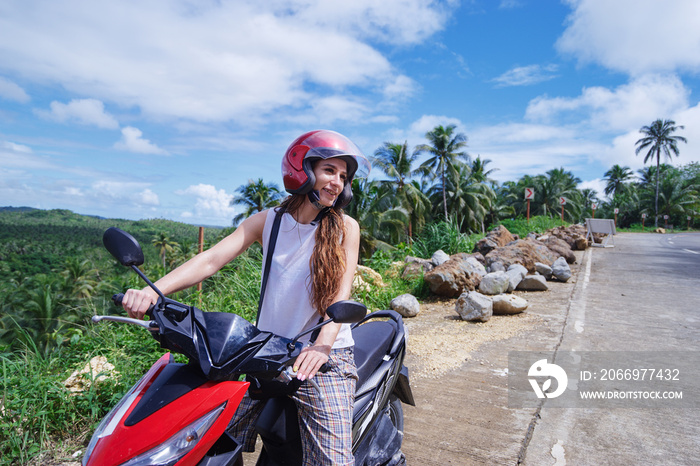 Tropical travel and transport. Young beautiful woman in helmet riding scooter on the road with palm trees.