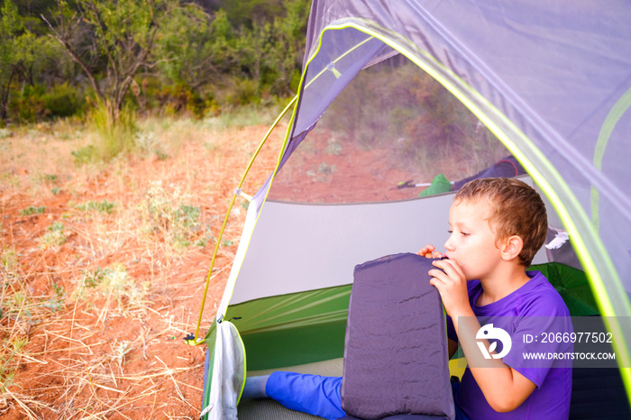 Camping boy, swelling his sleeping mat inside his tent.