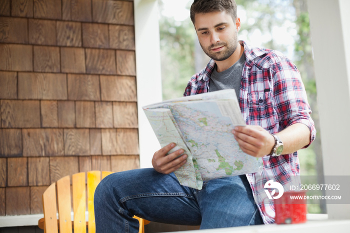 Young man sitting on cabin porch looking at map