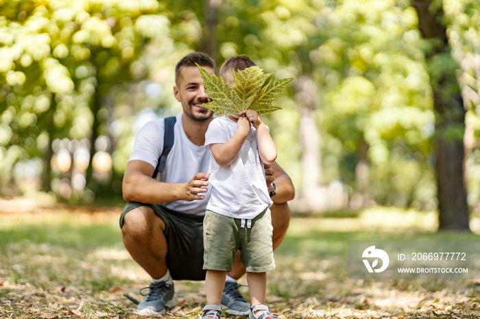 Vacation in the woods, family fun in the park, escape to nature and active weekend. A father and son are dressed in the same clothes. Boy holds a leaf in front of his face while dad posing for a photo