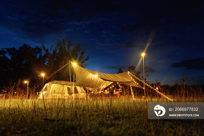 Outdoor camping tent with tarp or flysheet on grass courtyard and warm night light under dark blue sky twilight time, family vacation picnic on holiday relax. Ant eye view